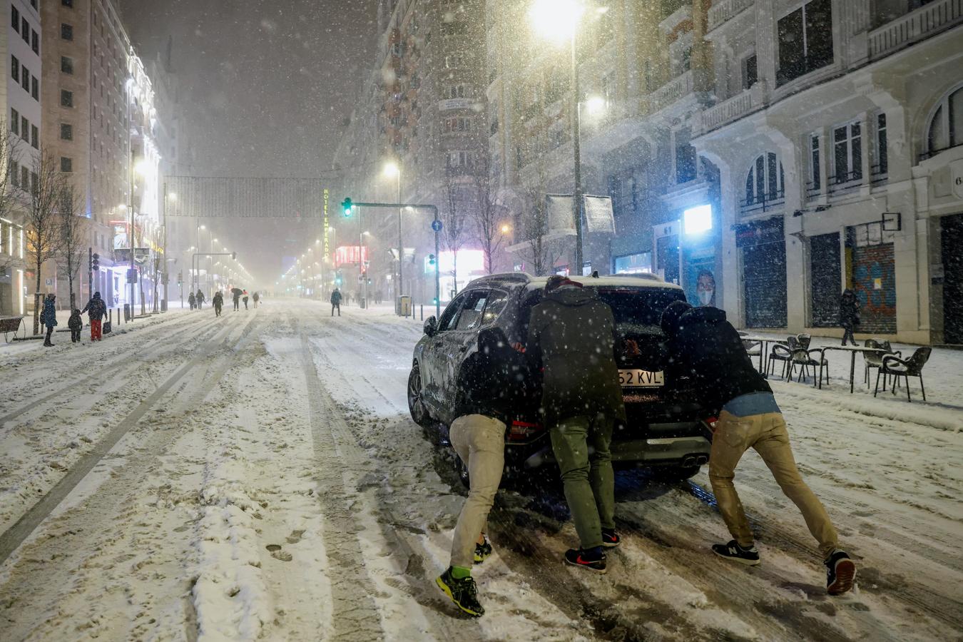 Coches atascados en la Gran Vía. Varias personas empujan un coche en la Gran Vía, en Madrid, en una jornada en la que la Agencia Estatal de Meteorología (Aemet) ha activado el nivel rojo.