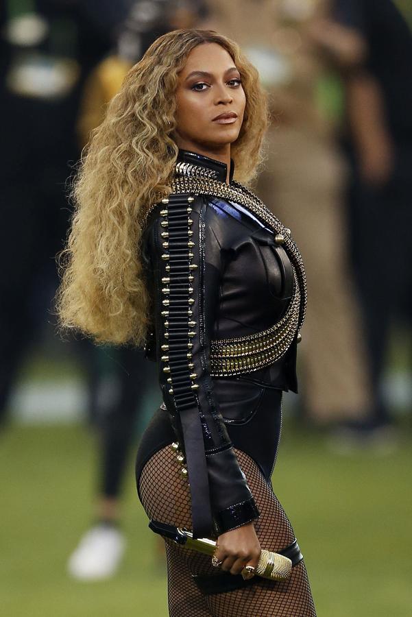 Beyoncé - 2013. Como suele ser habitual en sus actuaciones, se decantó por un body negro con detalles dorados firmado por Dsquared2. Poseía un aire militar gracias a las hombreras XXL con detalles tridimensionales que se prolongaban por las mangas y bandas cruzadas en el pecho. Remató su elección con unos botines con plataforma muy similares.