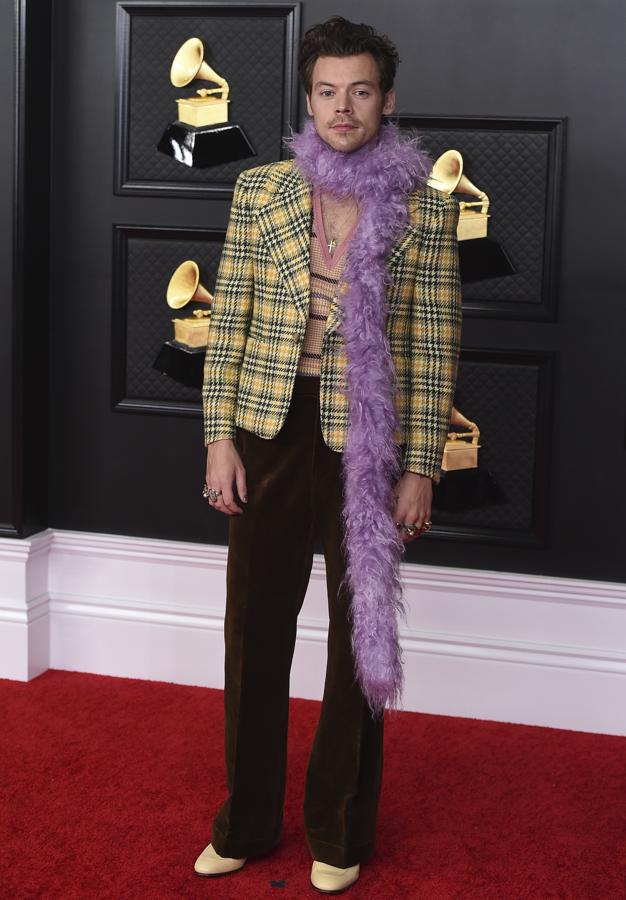 Harry Styles - Alfombra roja de los Grammy 2021. Como era de esperar el cantante apostó por su firma fetiche, Gucci, con un particular estilismo de aires setenteros compuesto por unos pantalones acampanados de terciopelo, chaqueta de tweed con grandes solapas y hombreras marcadas, jersey de punto con rayas en tonos pastel y cuello pico y una boa en color lila.