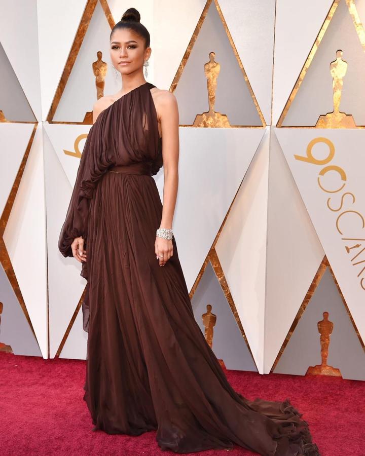 Zendaya en 2018 - Los vestidos más icónicos de los Oscar. El marrón es un color bastante olvidado en las alfombras rojas que sin embargo Zendaya supo defender a la perfección. Lo hizo con un vestido vaporoso de escote asimétrico e inspiración griega de Giambattista Valli Couture.