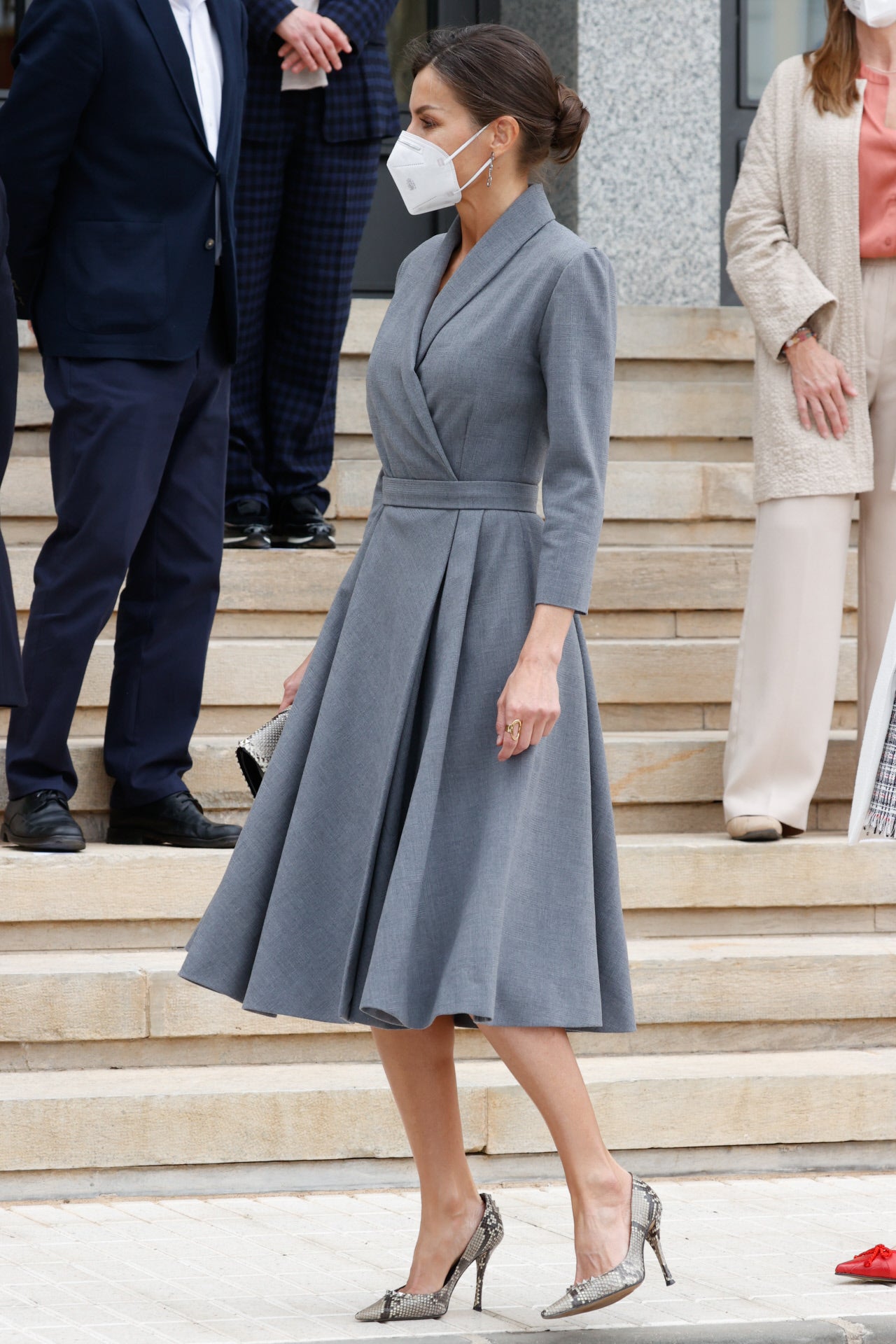 La Reina Letizia escogió un vestido gris cruzado con falda de vuelo a media pierna, sobrio y elegante. Este modelo ya lo ha llevado más veces, <a href="https://www.abc.es/estilo/moda/abci-dona-letizia-repite-total-look-favoritos-y-otra-leccion-estilo-202104121242_noticia.html">como es habitual en ella</a>, que reutiliza su armario y juega con los accesorios. En esta ocasión llevaba salones, un sobre de estampado animal a juego y el pelo recogido en un moño.. 