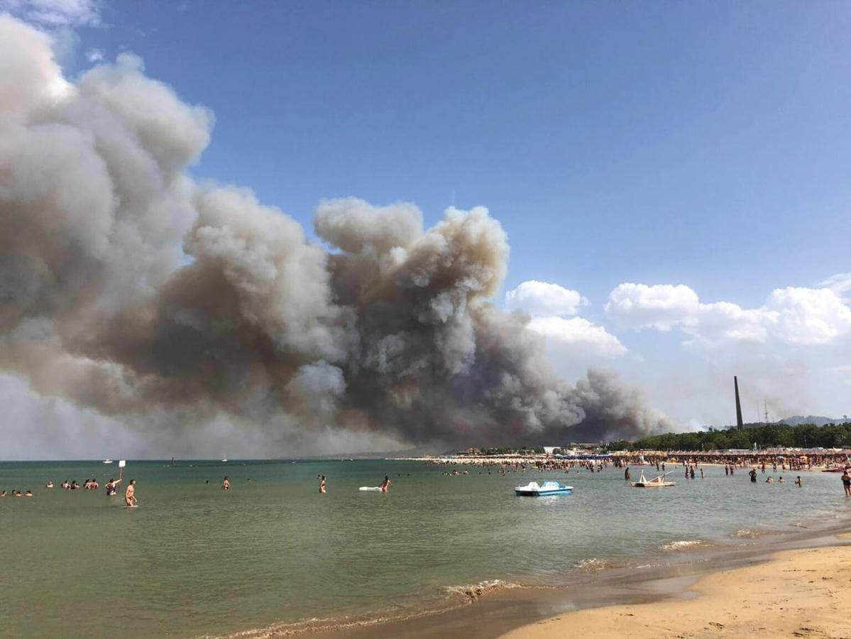 Bañistas observan desde las aguas de Pescara el humo del incendio en la reserva Dannunziana en Italia. 