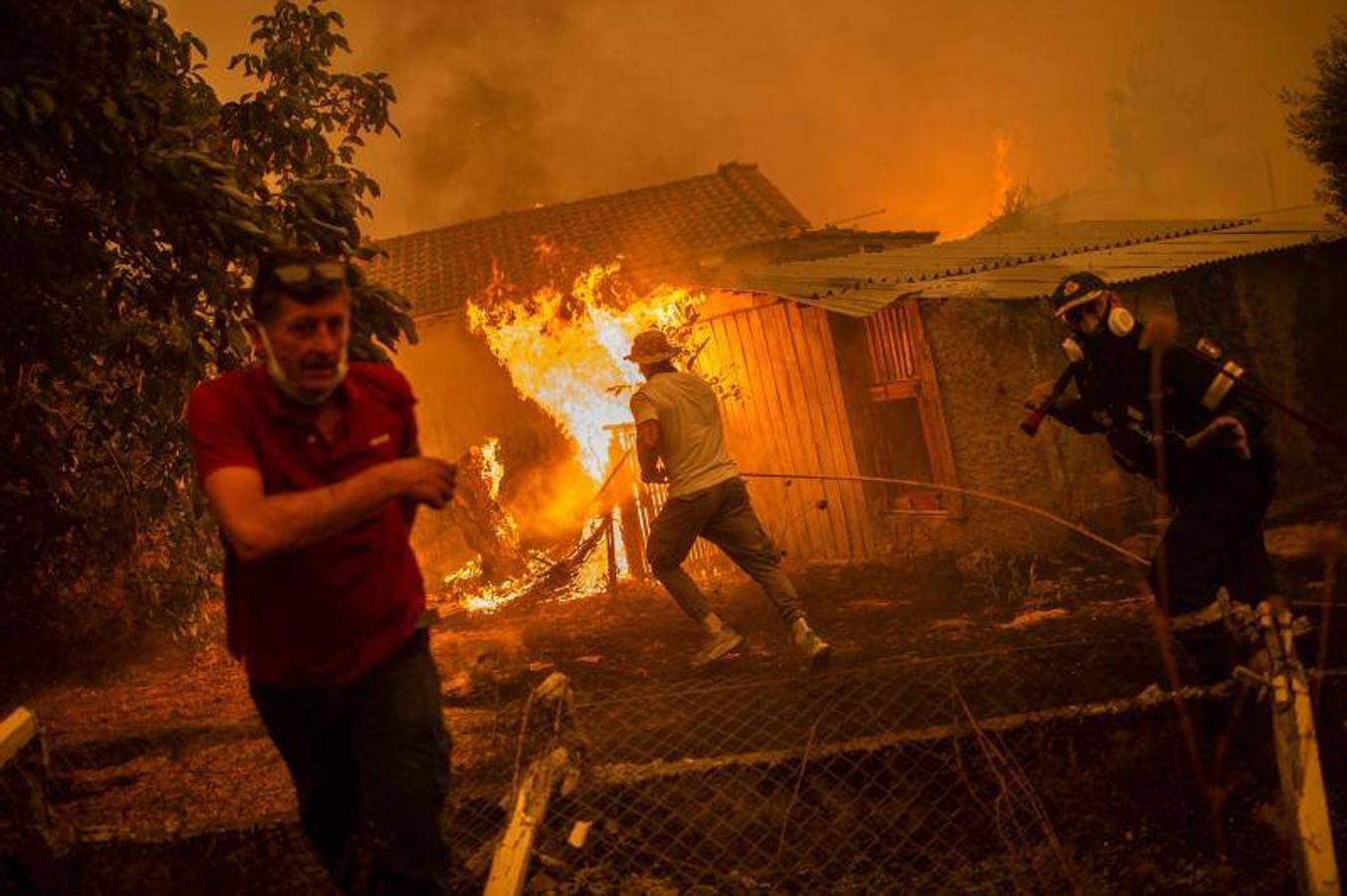 Un bombero y lugareños se apresuran a una casa en llamas en un intento de extinguir los incendios forestales que se acercan al pueblo de Pefki en la isla de Evia (Eubea). 