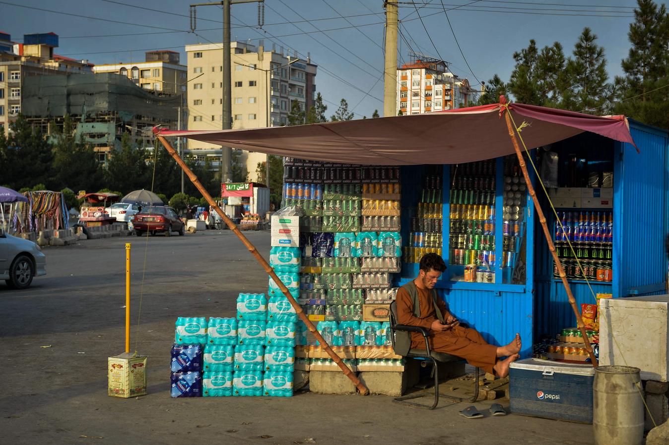 Un vendedor afgano se sienta junto a su tienda a lo largo de una carretera, esperando clientes en Kabul. 