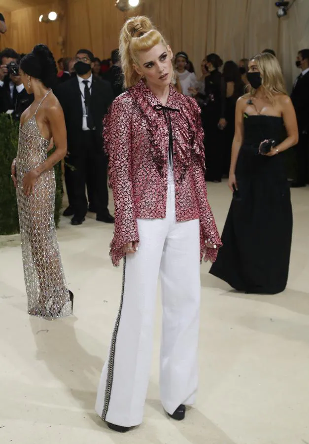 Kristen Stewart - Alfombra roja de la Gala MET 2021. Llevó un conjunto de Chanel compuesto por una camisa de lúrex con troquelados y chorreras en la parte delantera. Lo combinó con un pantalón fluido blanco con un bordado en el lateral y un recogido de aires retro.