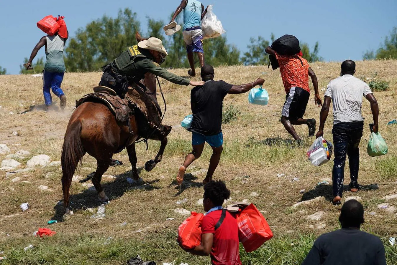 Agentes de la guardia fronteriza de  EE.UU. a caballo intentan evitar que un grupo de migrantes haitianos accedan al  campamento. 
