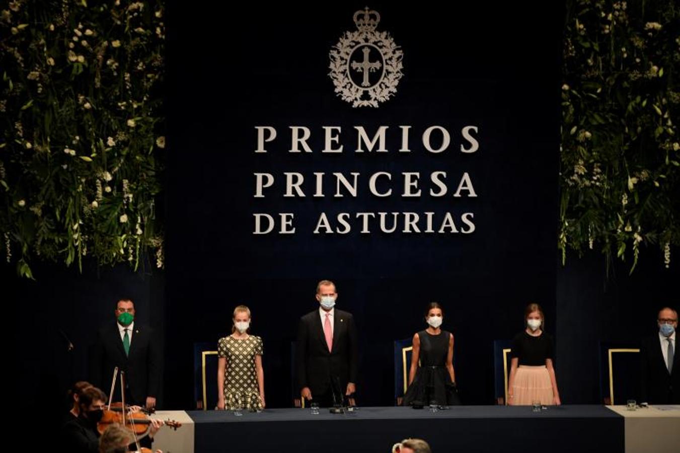 El Rey Felipe VI (3-i), la Reina Letizia (3-d), la Princesa Leonor (2-i), la Infanta Sofía (2-d) y el presidente del Principado, Adrián Barbón (i), escuchan el himno nacional. 