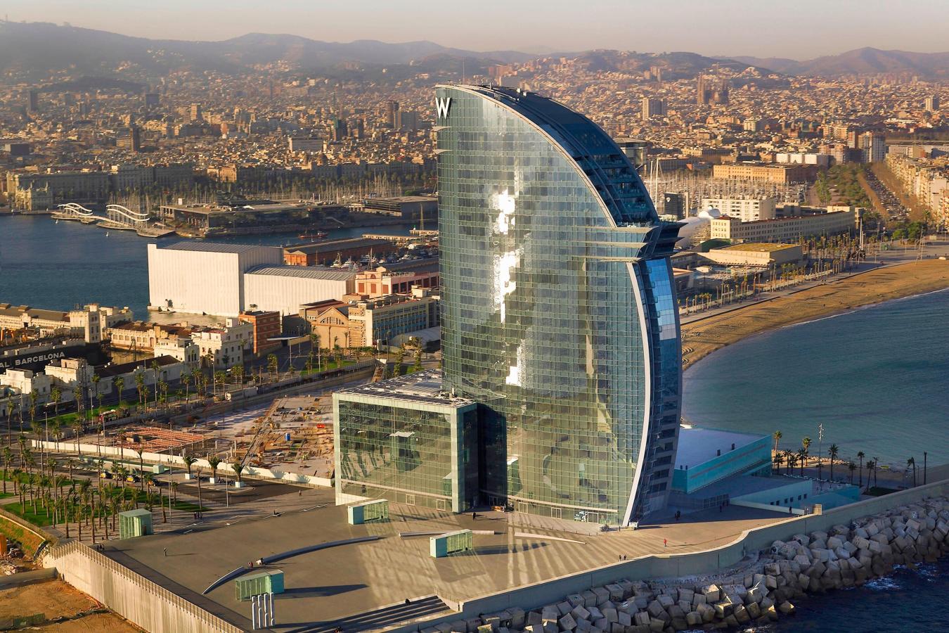 Mejor Hotel de Negocios de España 2021: W Barcelona. Diseñado por Ricardo Bofill, el W Barcelona es una maravilla arquitectónica y el escenario ideal para pasar una estancia inolvidable. Este alojamiento dispone de 473 habitaciones y suites con vistas panorámicas del Mediterráneo y la ciudad y de casi 7.000 metros cuadrados destinados a reuniones y eventos. Perfectos para relajarse después de un duro día de trabajo son su Spa y la zona de relajación GETAWAY. Además, los paladares más exigentes encontrarán en su restaurante La Barra de Carles Abellán, con una estrella Michelin, el mejor espacio gourmet para degustar exquisitos platos. Y para el afterwork es el Eclipse Bar, un exclusivo cocktail lounge situado en lo alto del hotel, en el piso 26.