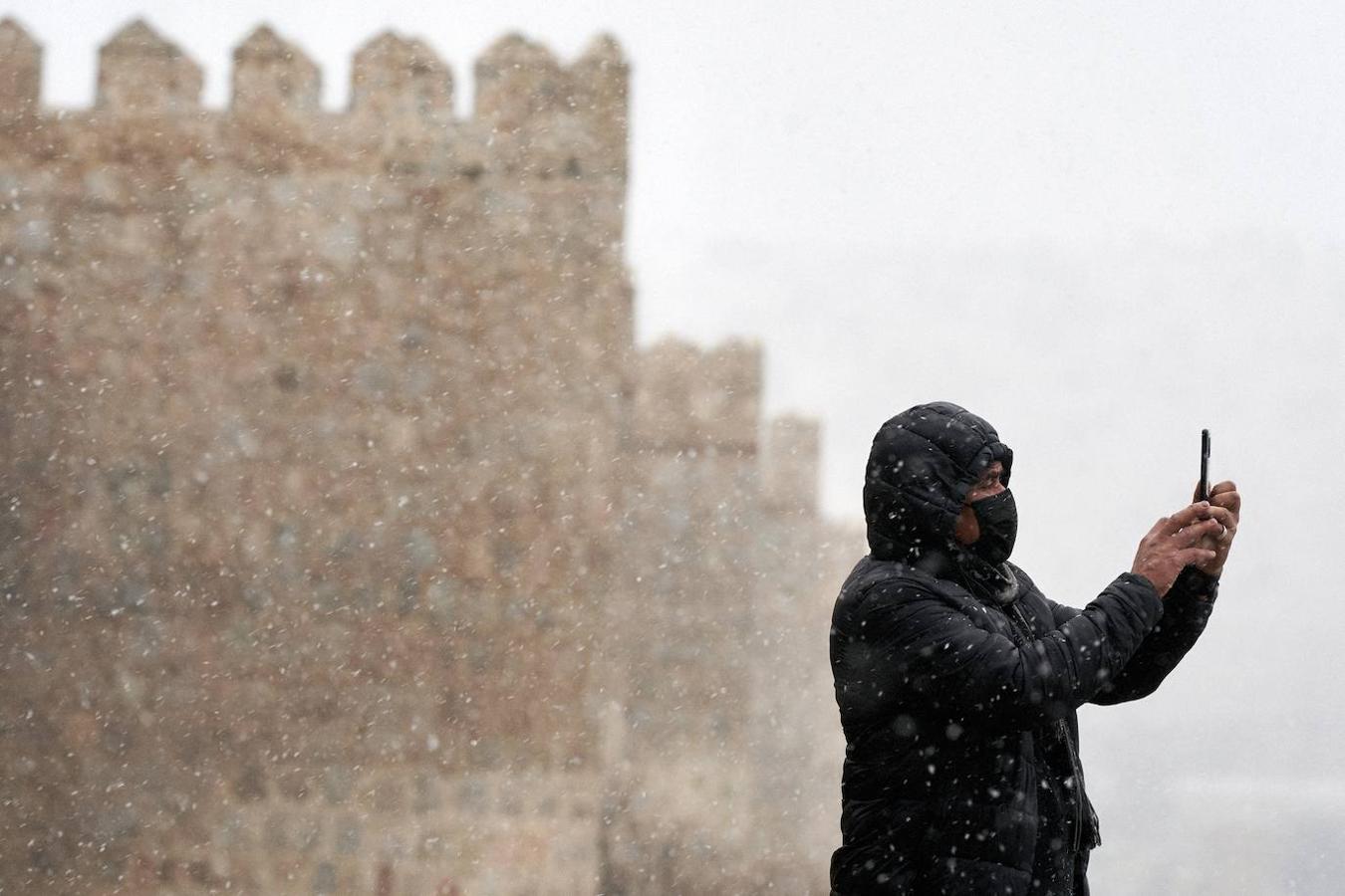 Un hombre se hace una foto con su teléfono móvil junto a la muralla de Ávila durante la primera nevada del otoño en la capital abulense. 