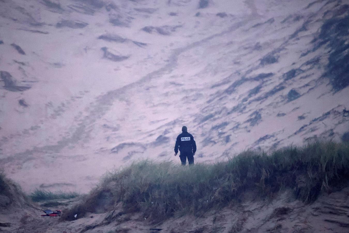 Un agente de la policía francesa se queda paralizado viendo desde las dunas cómo las personas se apresuran en subirse al bote. 