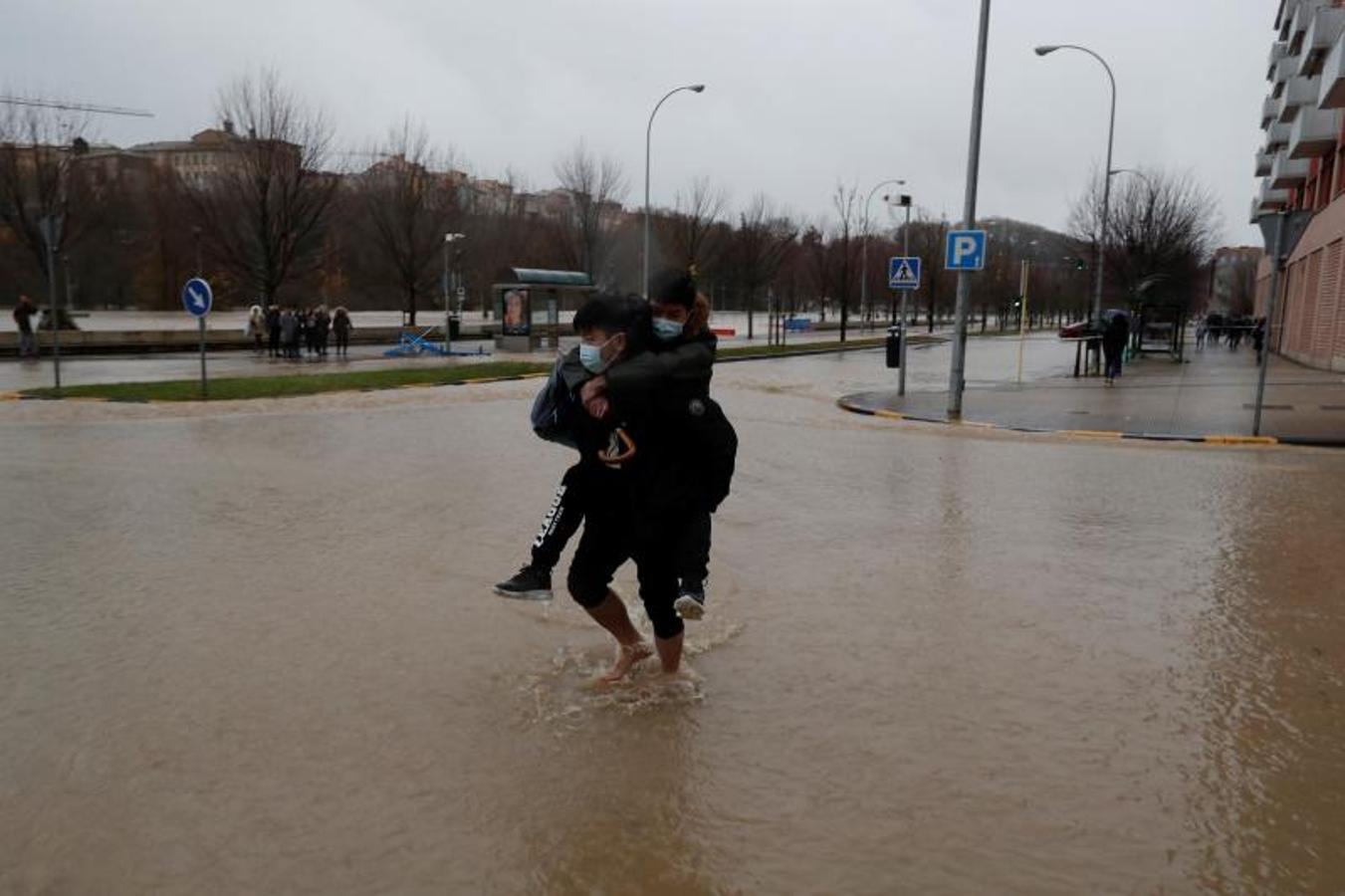 Un hombre carga con un joven a la espalda para cruzar algunas calles inundadas por el desbordamiento del río Arga a su paso por el barrio de la Rochapea en Pamplona. 