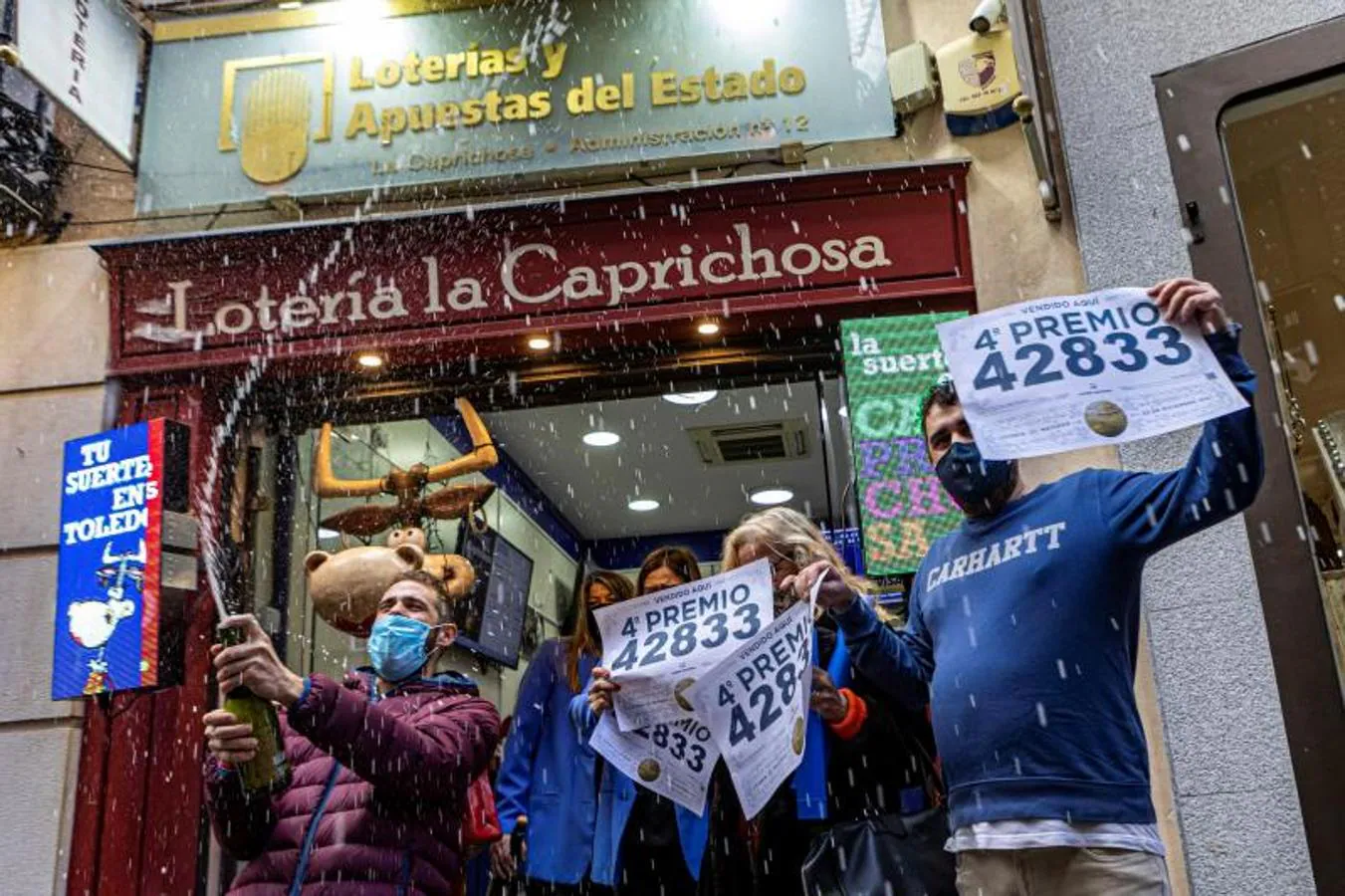Trabajadores de la administración La Caprichosa de Toledo muestran el cartel de venta del número 42833 de la lotería que ha sido agraciado con el cuarto premio. 