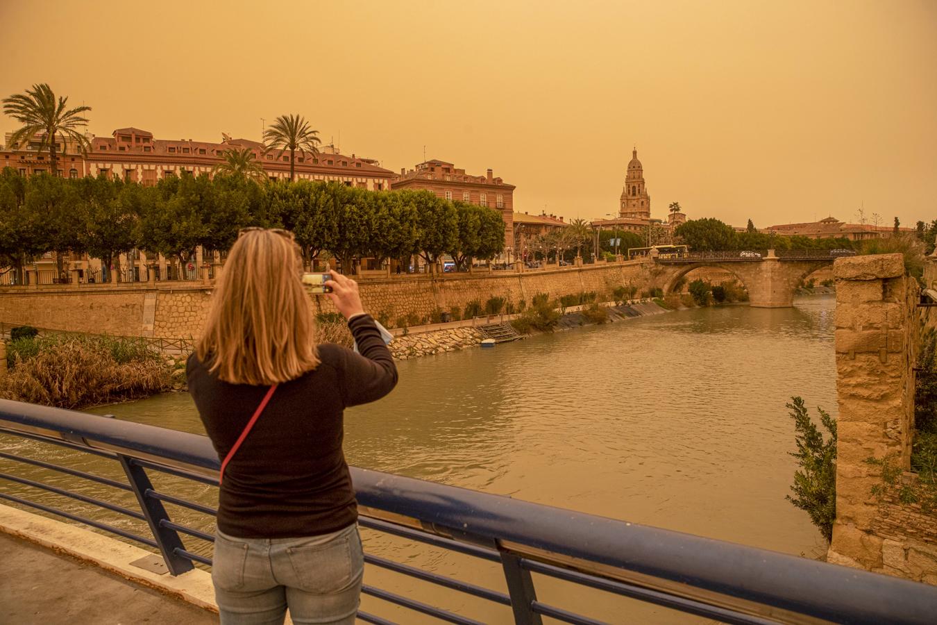 Murcia se tiñe de naranja. Una mujer hace una fotografía con su móvil del aspecto que presentaba la ciudad de Murcia en la tarde del lunes 14 de marzo