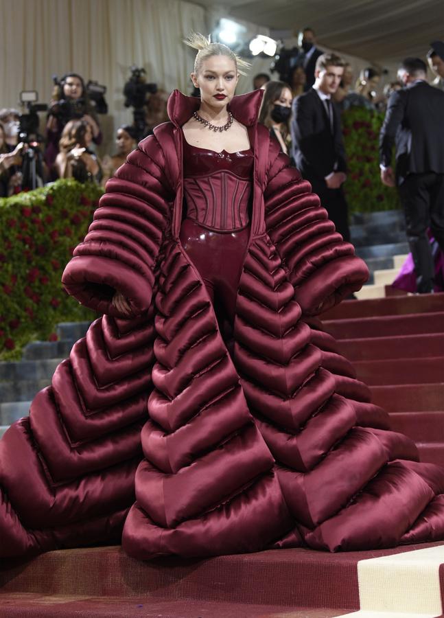 Gigi Hadid - Alfombra roja de la Gala MET 2022. Lució un mono de látex burdeos con cuerpo encorsetado que conjuntó con un plumas XXL de Versace.