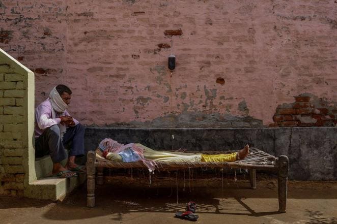 Un hombre se sienta junto a su esposa, que sufría de fiebre alta, mientras ella recibe líquido de rehidratación por vía intravenosa en una clínica improvisada en la aldea de Parsaul, ubicada en el estado norteño de Uttar Pradesh, el 22 de mayo de 2021