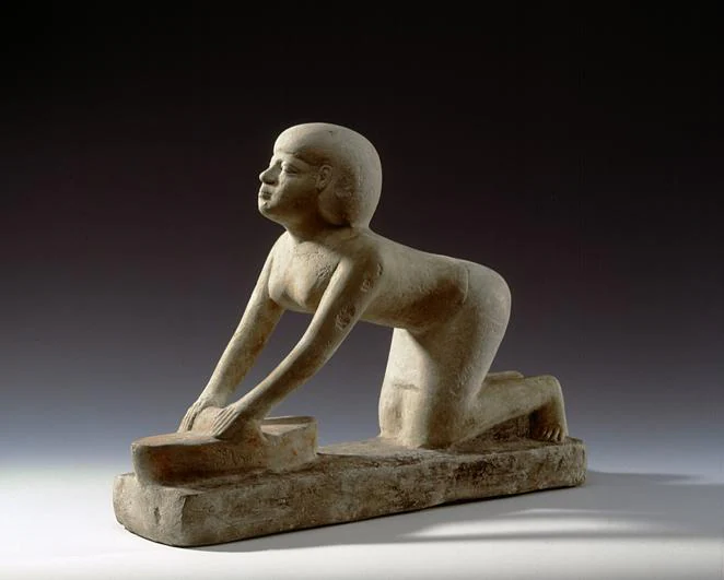 Trabajadora. Una figura de piedra caliza de una molinera del Reino Antiguo (2686-2181 a.C.) del museo de Hildesheim en la que se ve a una mujer arrodillada e inclinada ante una muela en la que tritura el grano con ayuda de una gran piedra