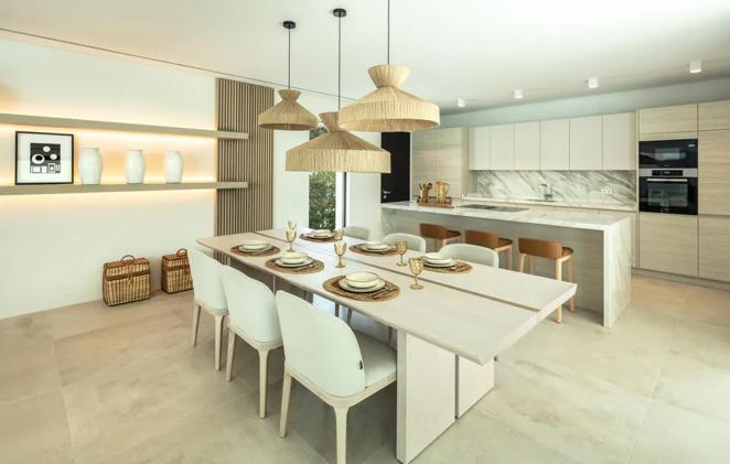 La cocina se integra con el comedor y está decorada en tonos blancos y marrones. Gracias a los ventanales cuenta con mucha luz natural, apoyada por focos y lámparas de inspiración mediterránea.