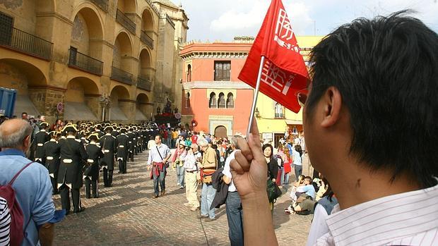 Un grupo de turistas observa una banda al paso junto a la Catedral durante la Semana Santa