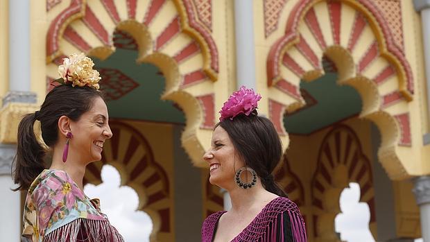 Dos mujeres ataviadas con traje de gitana delante de la Portada de la Feria