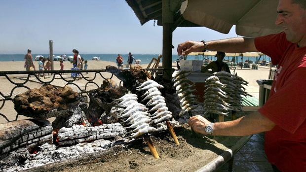 Un hombre asa sardinas en un espeto en una playa malagueña