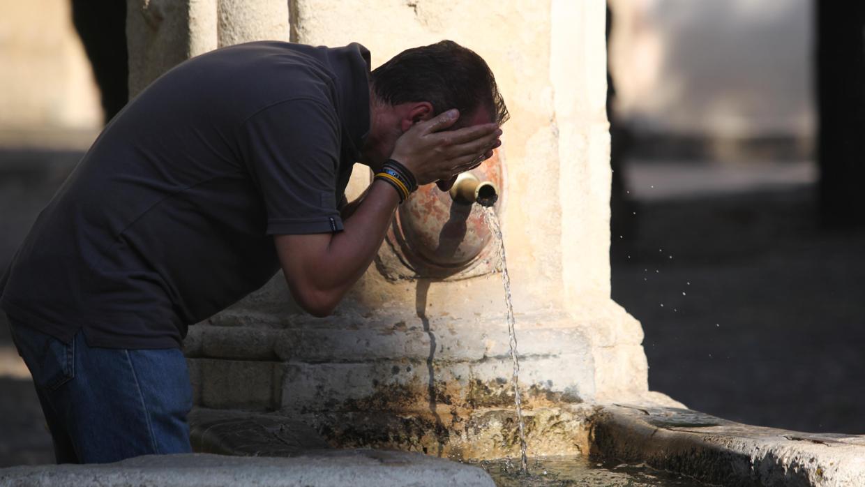 Un hombre se refresca la cara y la cabeza en una fuente