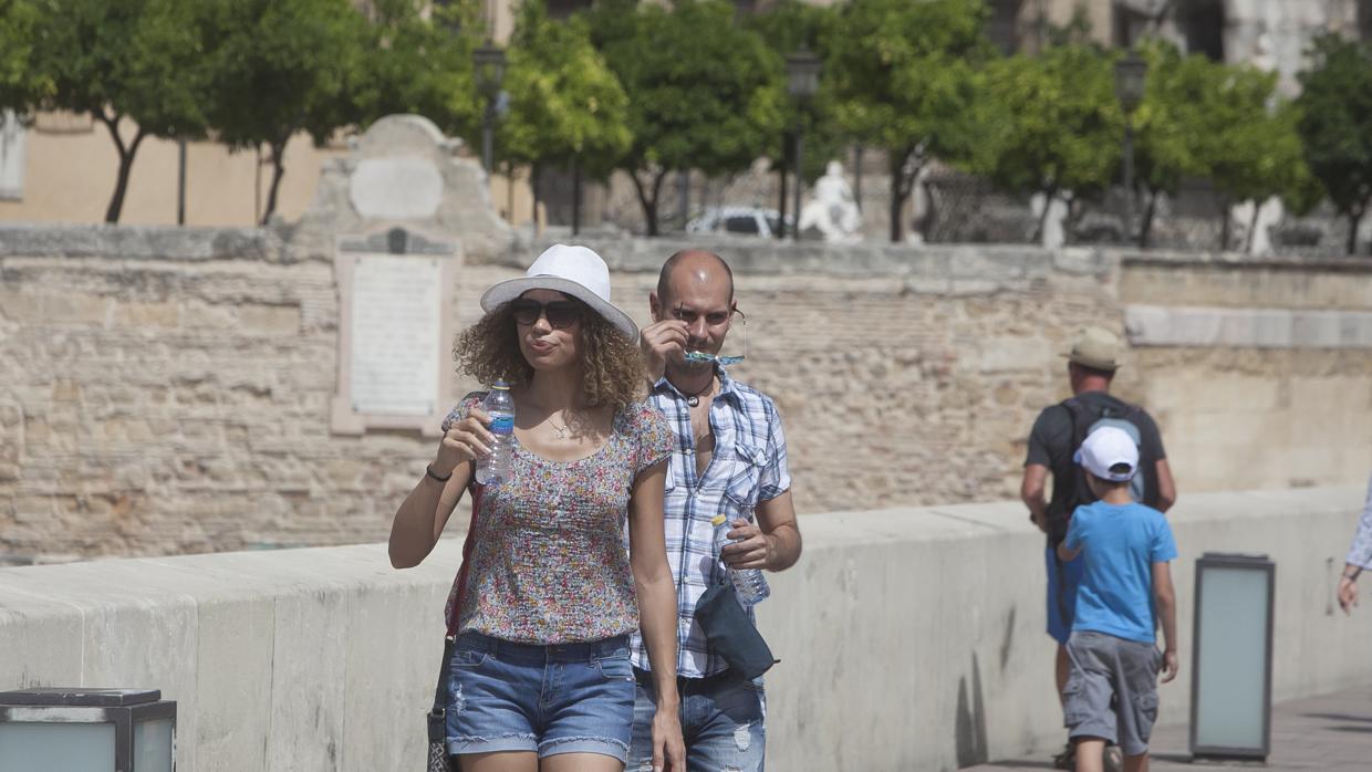 Una mujer camina por Córdoba con sombrero y botella de agua para prevenir los efectos del calor