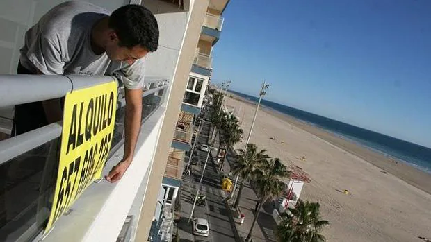 Un hombre coloca el cartel de alquiler en un piso en la playa