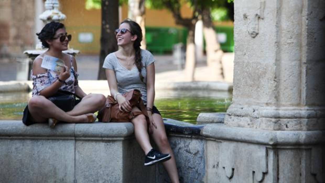 Dos turistas descansan del calor en una fuente.