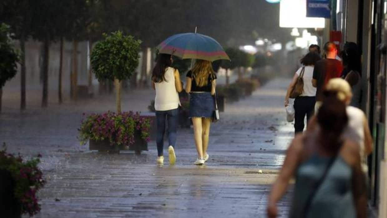 Dos chicas se resguardan de la lluvia bajo un paraguas un día de calor