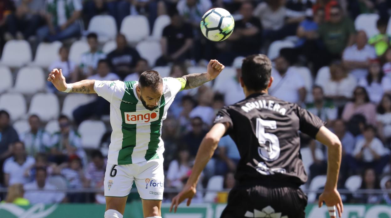 El pivote del Córdoba Edu Ramos despeja el balón con la cabeza ante Aguilera, del Huesca