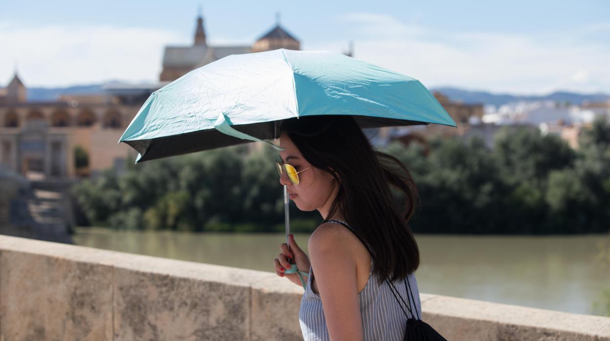 Una mujer se protege del sol con un paraguas en el Puente Romano de Córdoba