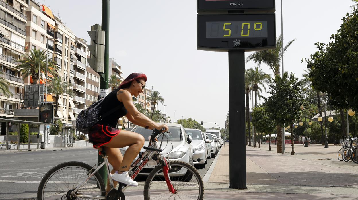 Una mujer pasa en bicicleta ante un termómetro que marca los 50 grados