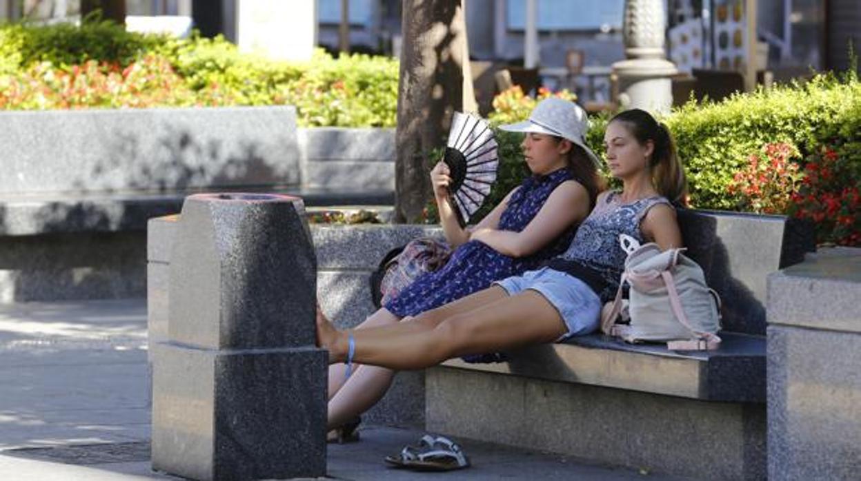 Dos jóvenes se resguardan del calor en un banco de la plaza de Las Tendillas de Córdoba