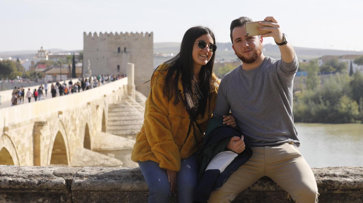 Una pareja de jóvenes turistas se fotografía con el Puente Romano y la Torre de la Calahorra al fondo