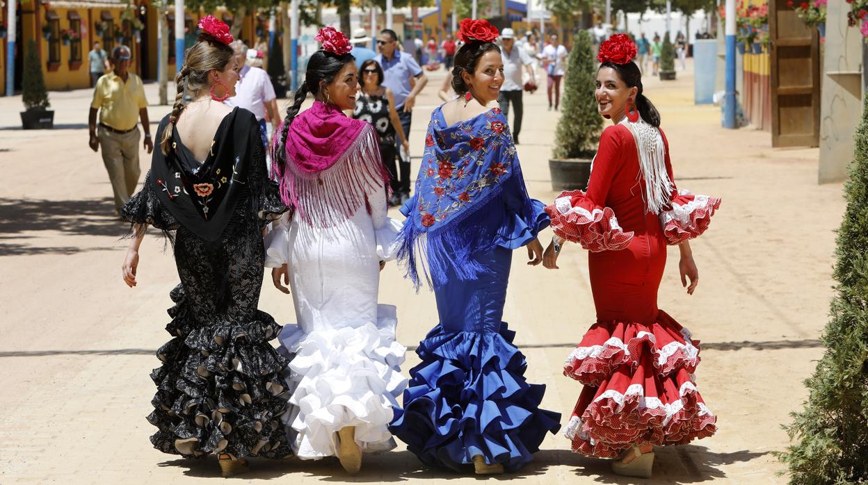 Cuatro jóvenes vestidas de flamenca avanzan por la Feria de Córdoba