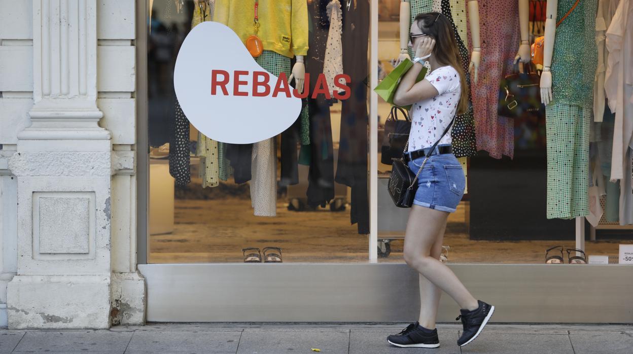 Una joven pasa delante de una céntrica tienda de Córdoba que luce el cartel de rebajas