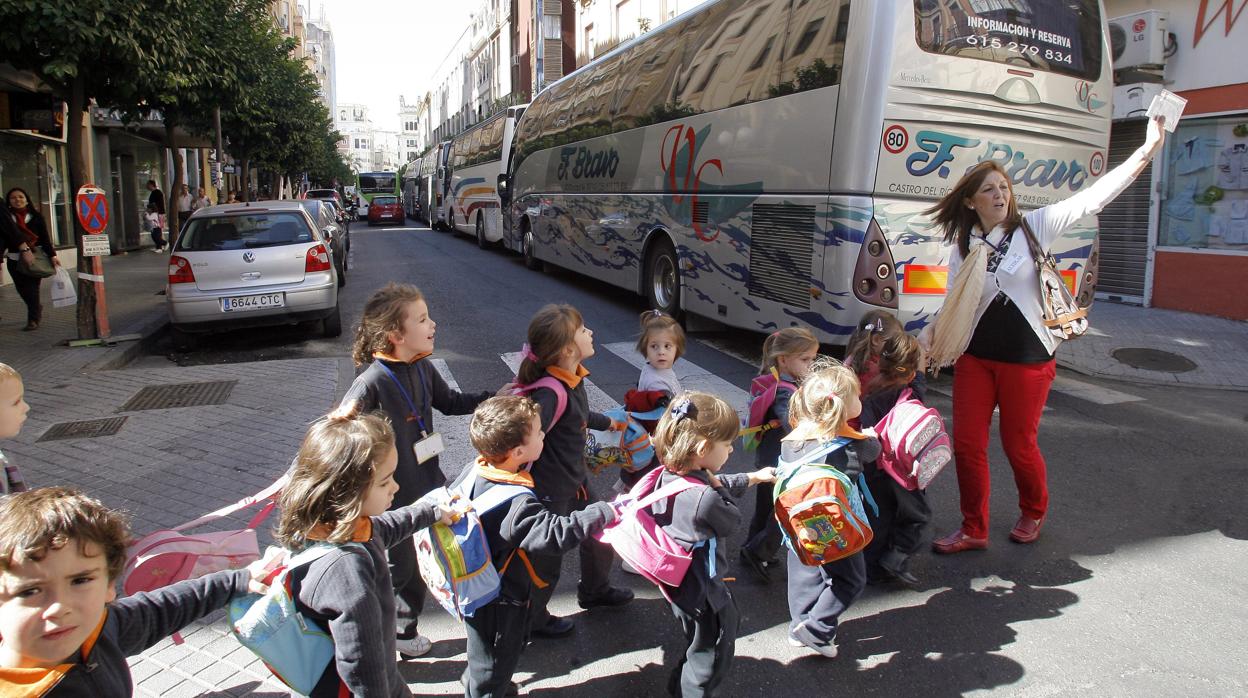 Una monitora de «Camino al cole» conduce a un grupo de niños, junto a un autobus escolar en Claudi Marcelo