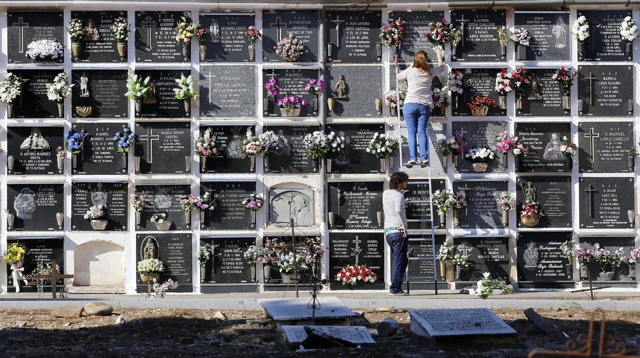 Dos personas adecentan una tumba en el cementerio de la Salud