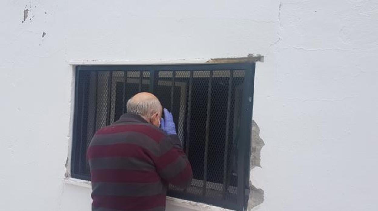 Un vecino mira por la ventana forzada para robar en las instalaciones de Cáritas en Aguilar de la Frontera