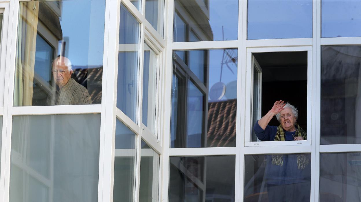 Dos personas mayores miran por la ventana de la residencia en la que viven