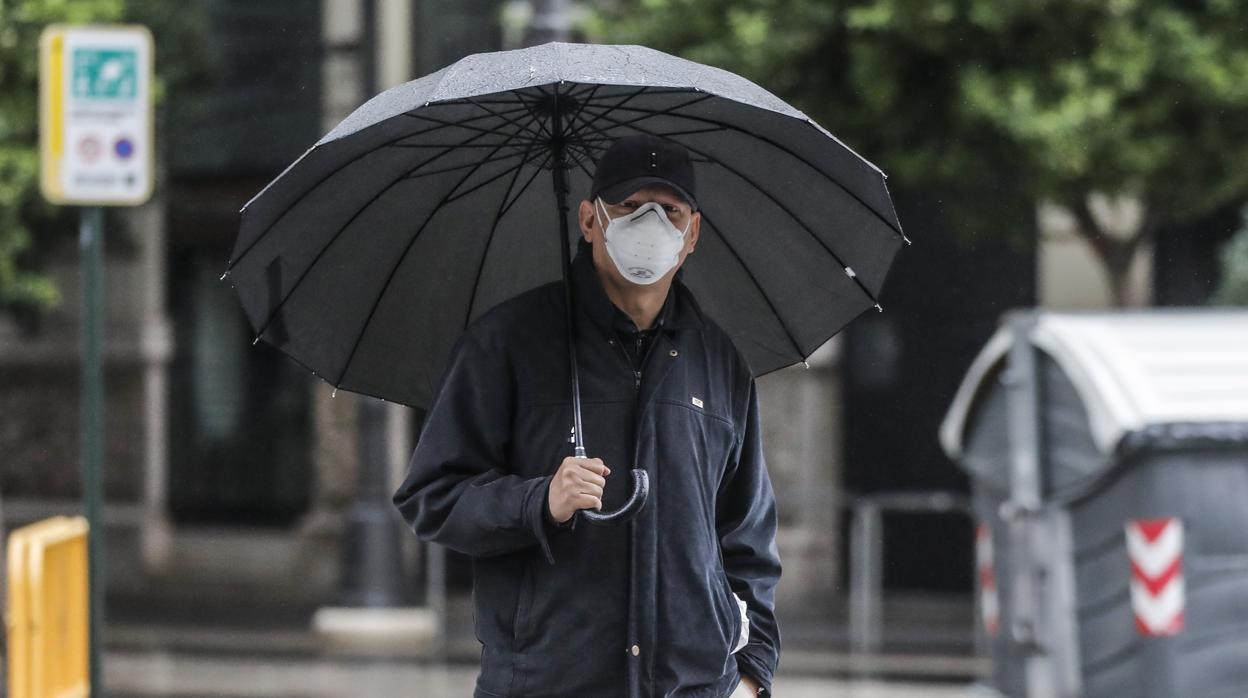 Un hombre con paraguas y mascarilla