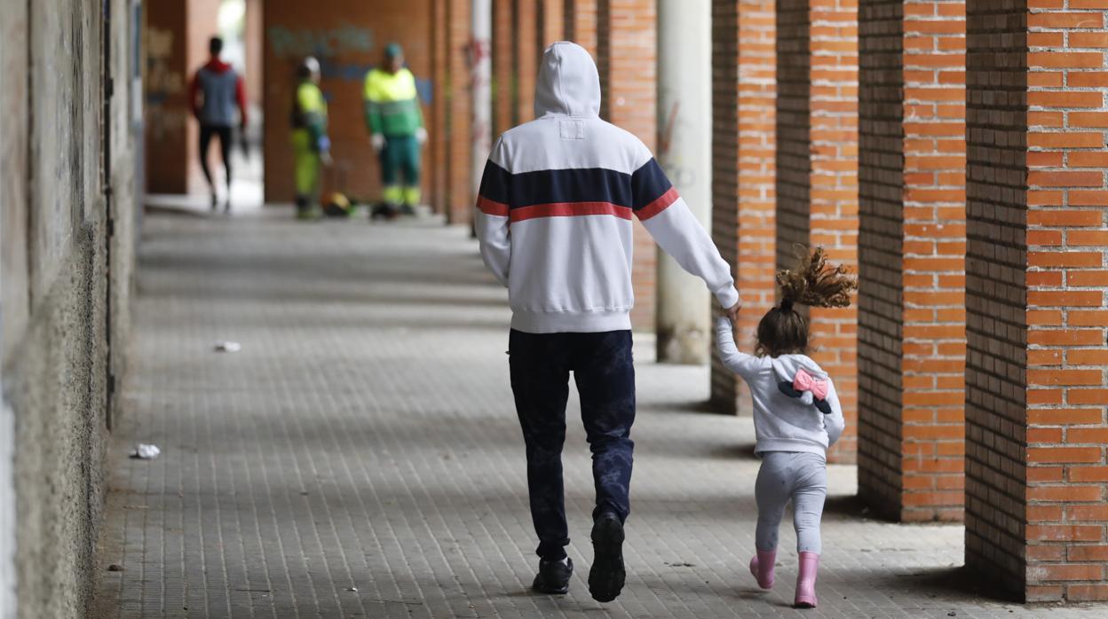 Un hombre lleva a una niña de la mano por los soportales del barrio de Moreras en Córdoba