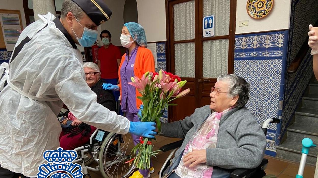 Un policía nacional entrega un ramo a una de las mayores de este geriátrico