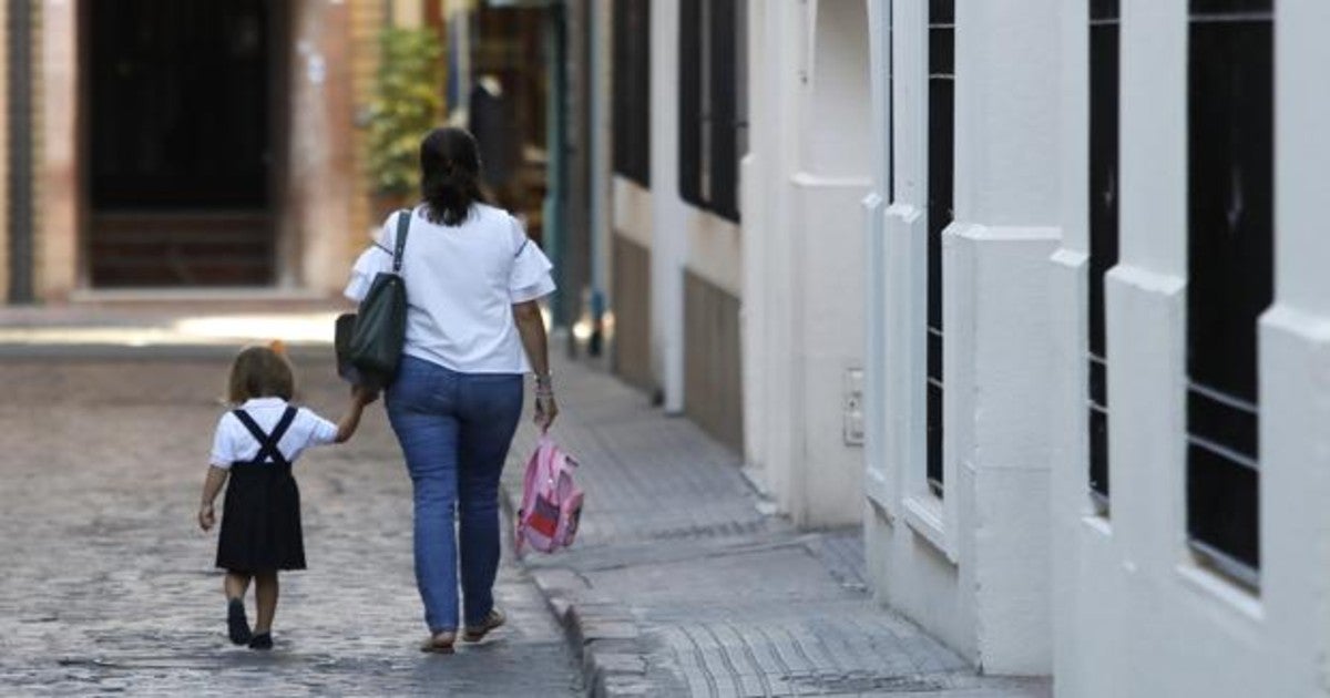 Una madre camina con su hija de la mano hacia el colegio por una calle de Sevilla