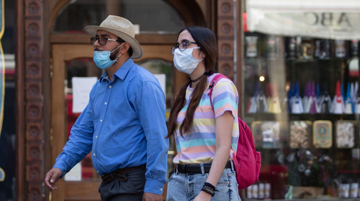 Dos personas con mascarilla -él, mal puesta porque no le cubre la nariz-, por las calles de Sevilla