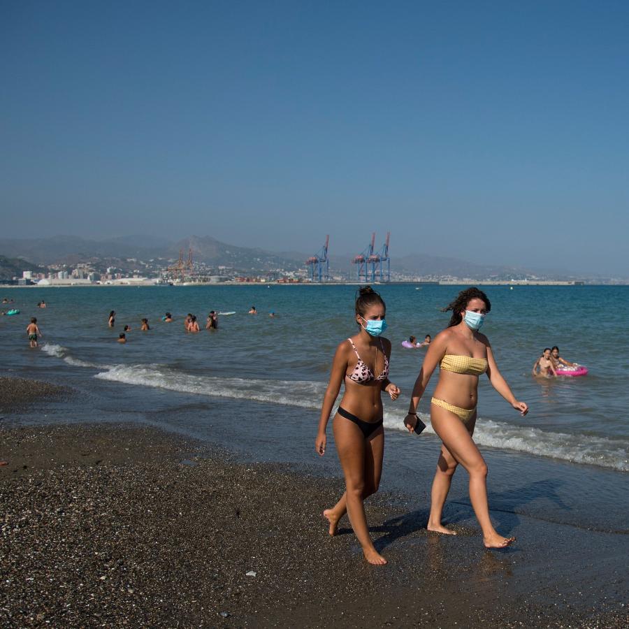 Bañistas con mascarillas pasean por la orilla de la playa de la Misericordia en Málaga ante la mirada de un vigilante de la Junta