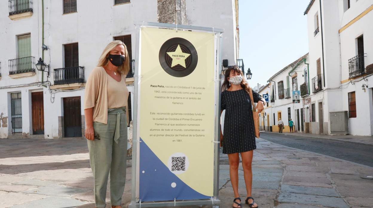 Isabel Albás y Lucia del Pino posan junto al cartel de Paco Peña