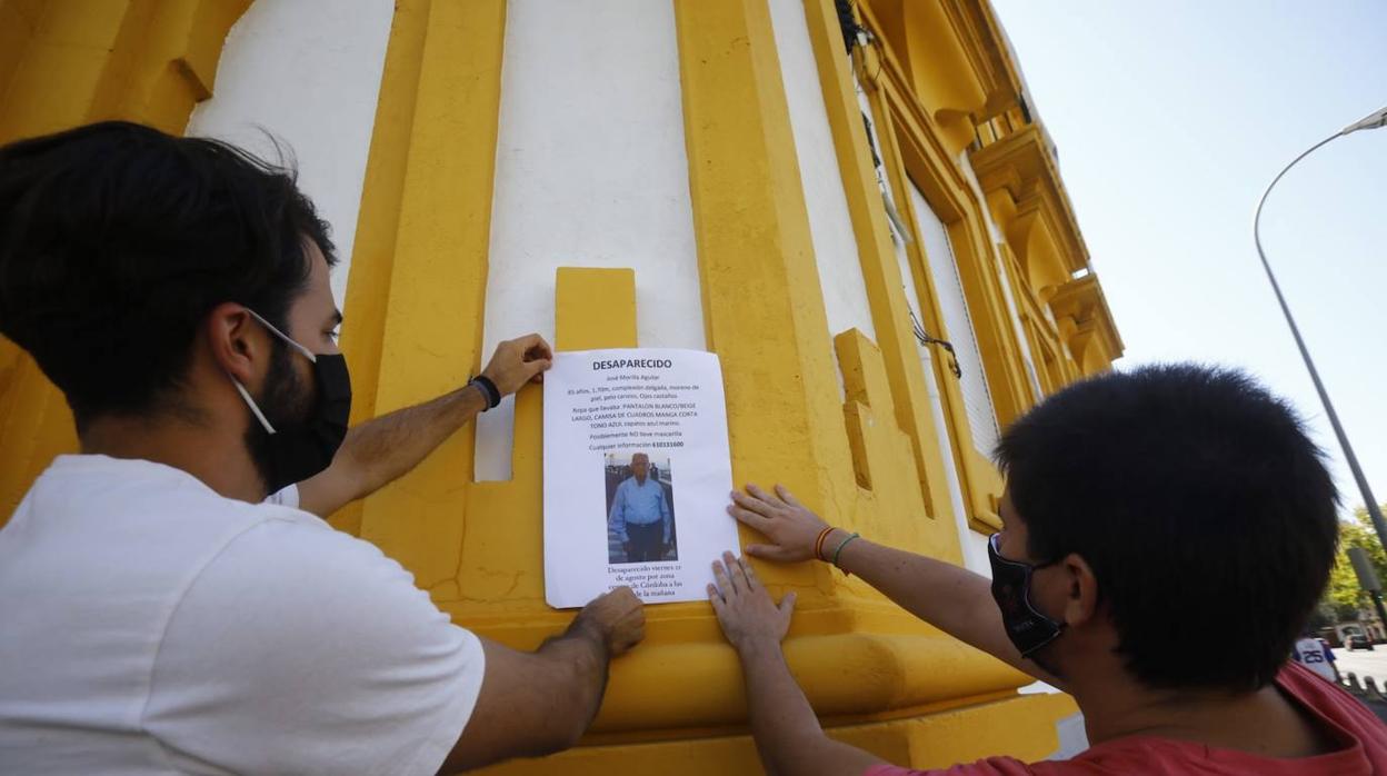 Dos familiares pegan en la fachada de un edificio un cartel con la foto del desaparecido