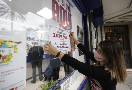 Una empleada del despacho de Loterías del Estado coloca el cartel que anuncia el premio