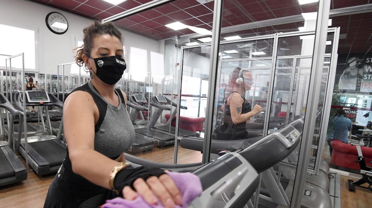 Una usuaria protegida con mascarilla desinfecta una cinta de correr al final de una sesión de entrenamiento en un gimnasio